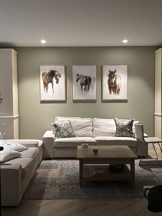Oil paintings of horses displayed in a private residence, three works in matching frames above a sofa.