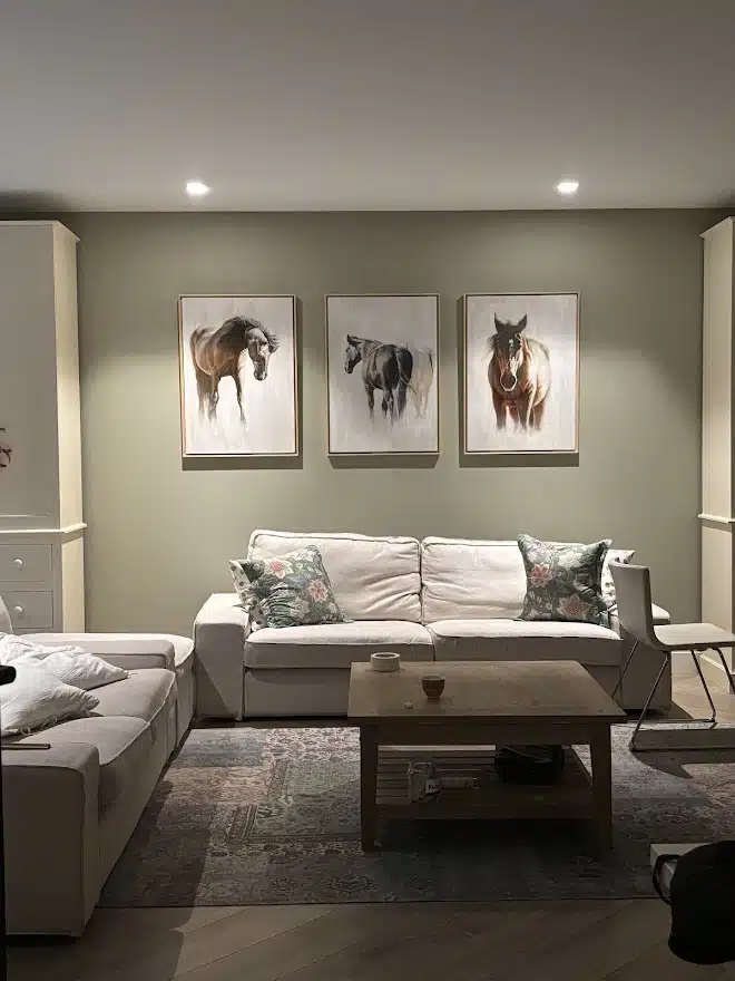 equine-paintings-private-collection Oil paintings of horses displayed in a private residence, three works in matching frames above a sofa.